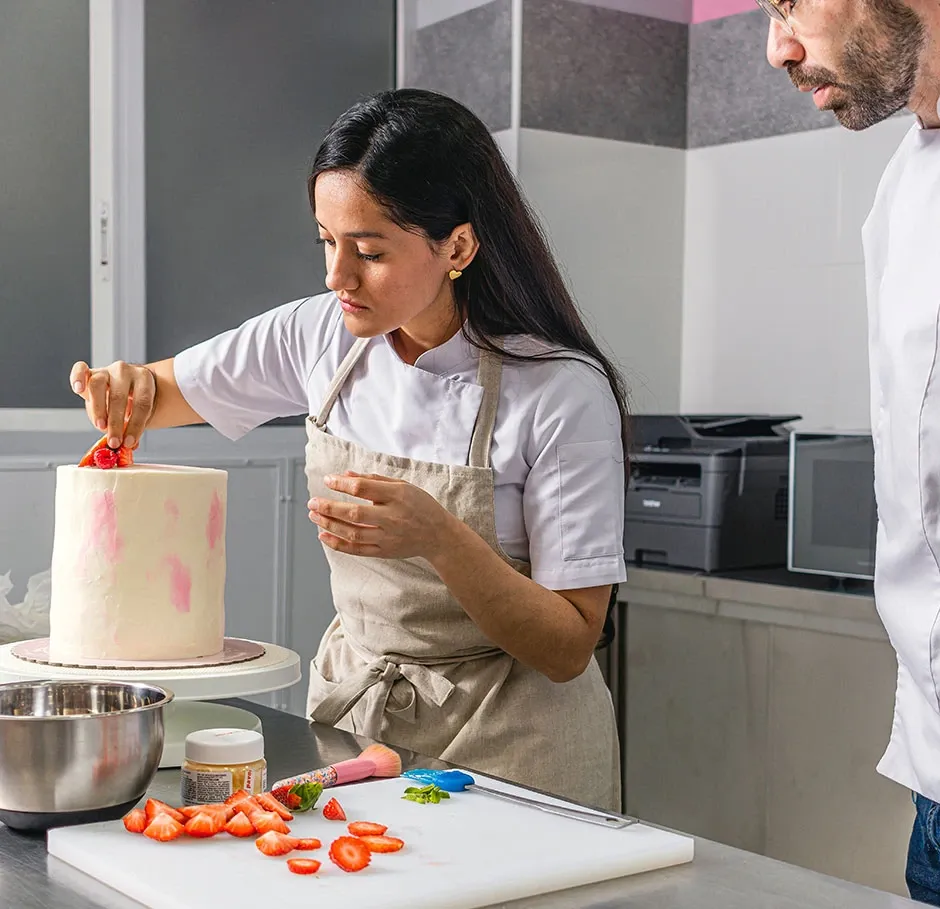 Apprenante en formation pâtisserie décorant un gâteau à la fraise sous la supervision d’un formateur, dans le cadre d’un parcours CAP pro