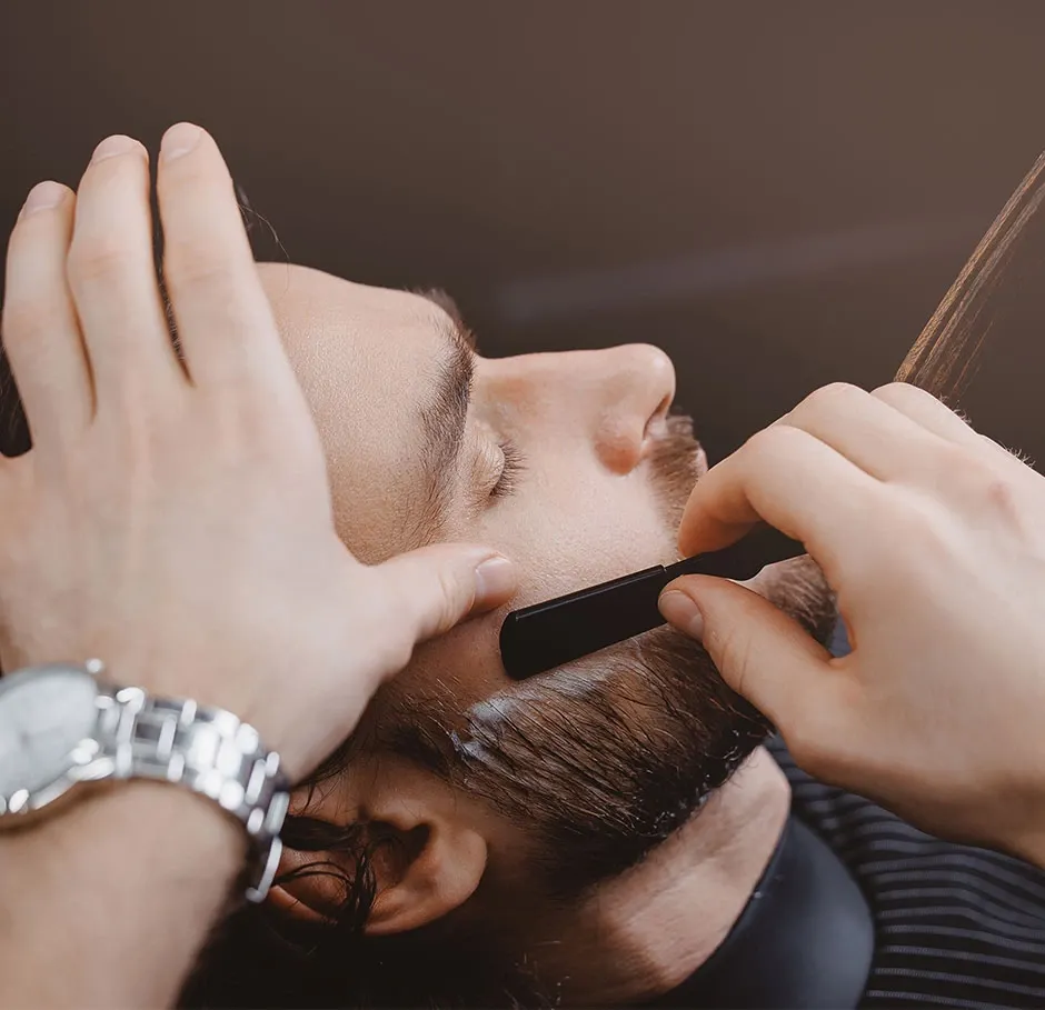 Apprenant en formation coiffure pratiquant le rasage et la taille de barbe avec un coupe-choux sur un modèle en atelier professionnel